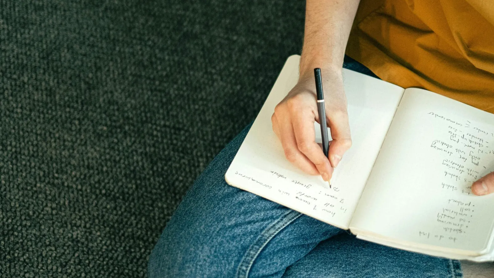 A person writing in a notebook resting on their lap