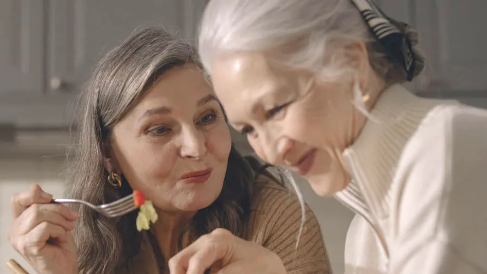 Two women tasting food together in a kitchen